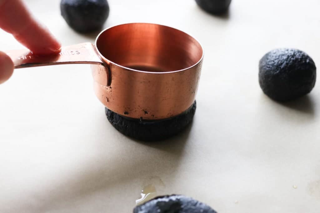 pushing a measuring cup into a fresh milled homemade oreo ball to flatten it