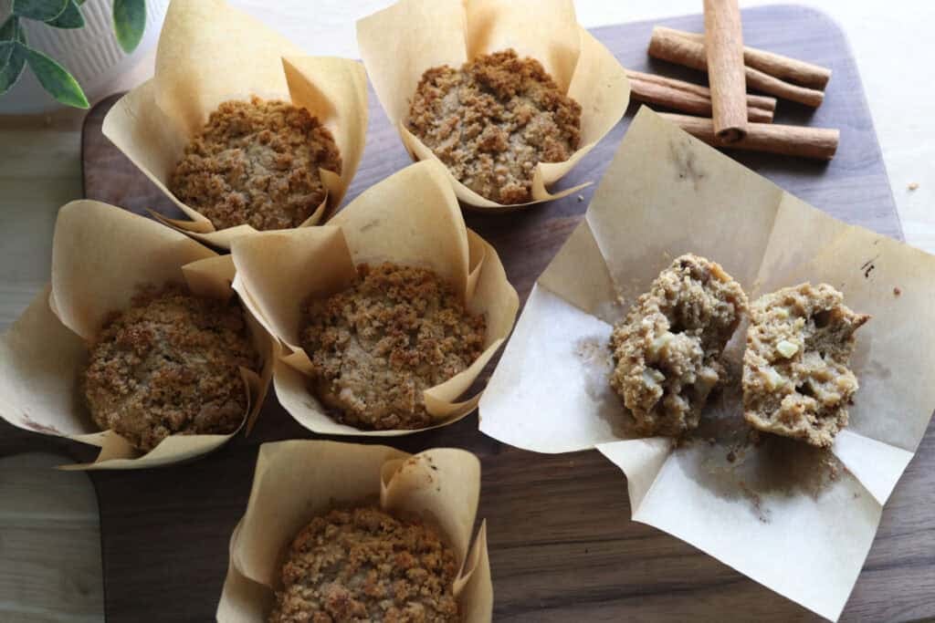 Freshly milled apple cinnamon streusel muffins on a cutting board with one muffin cut in half