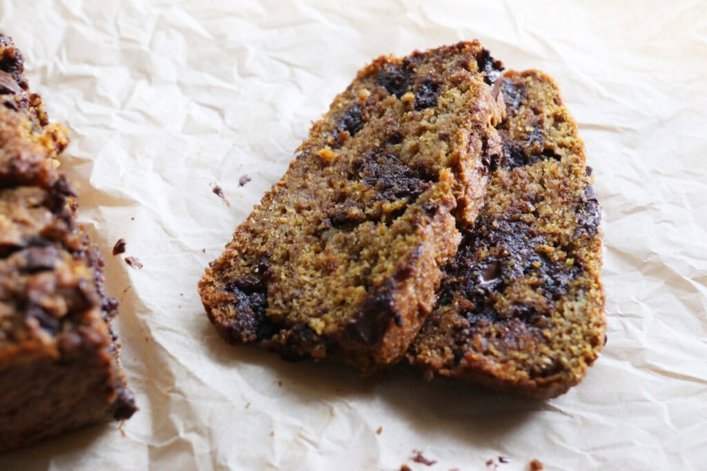 two pieces of fresh milled pumpkin banana bread with chocolate chips on parchment paper