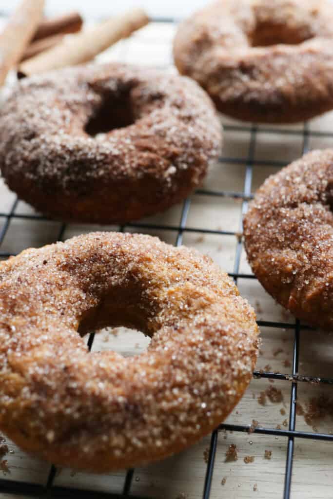a fresh milled cinnamon sugar pumpkin cake donut covered in a cinnamon sugar mixture on a wire rack