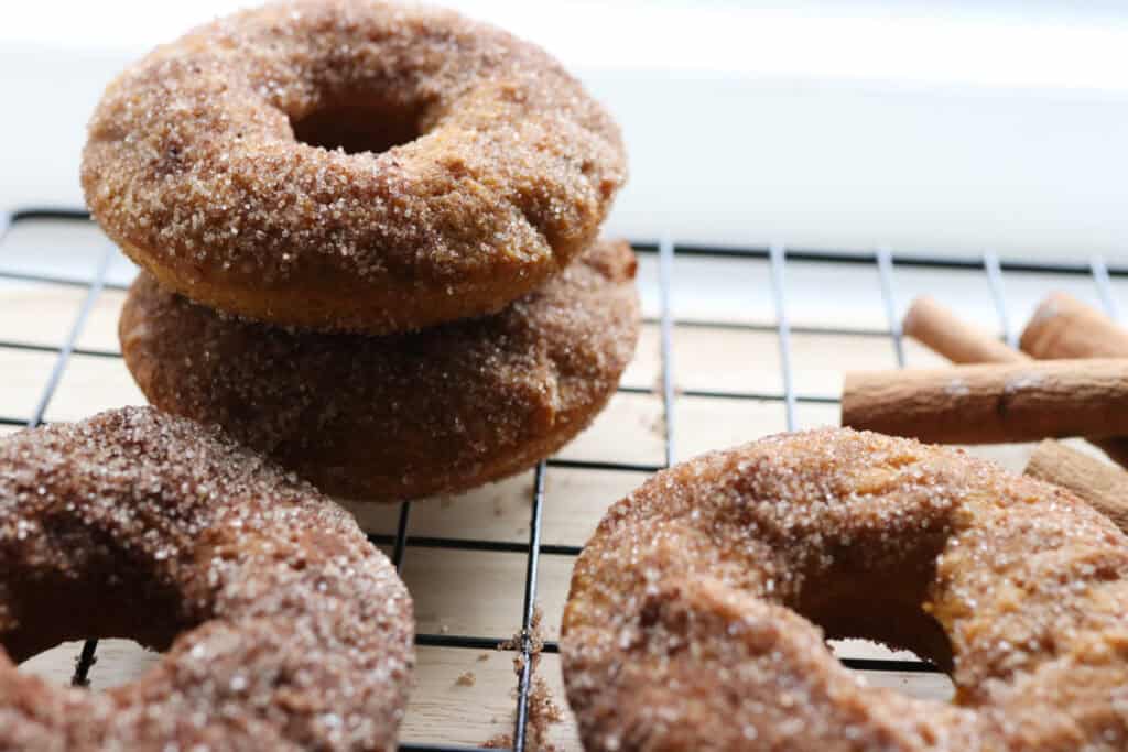 fresh milled pumpkin cake donuts with cinnamon sugar on them stacked on top of each other