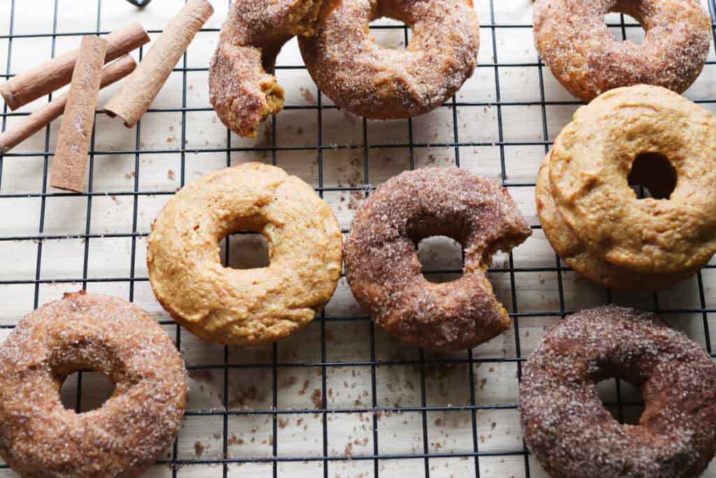 fresh milled cinnamon sugar pumpkin cake donuts on a wire rack with cinnamon sticks