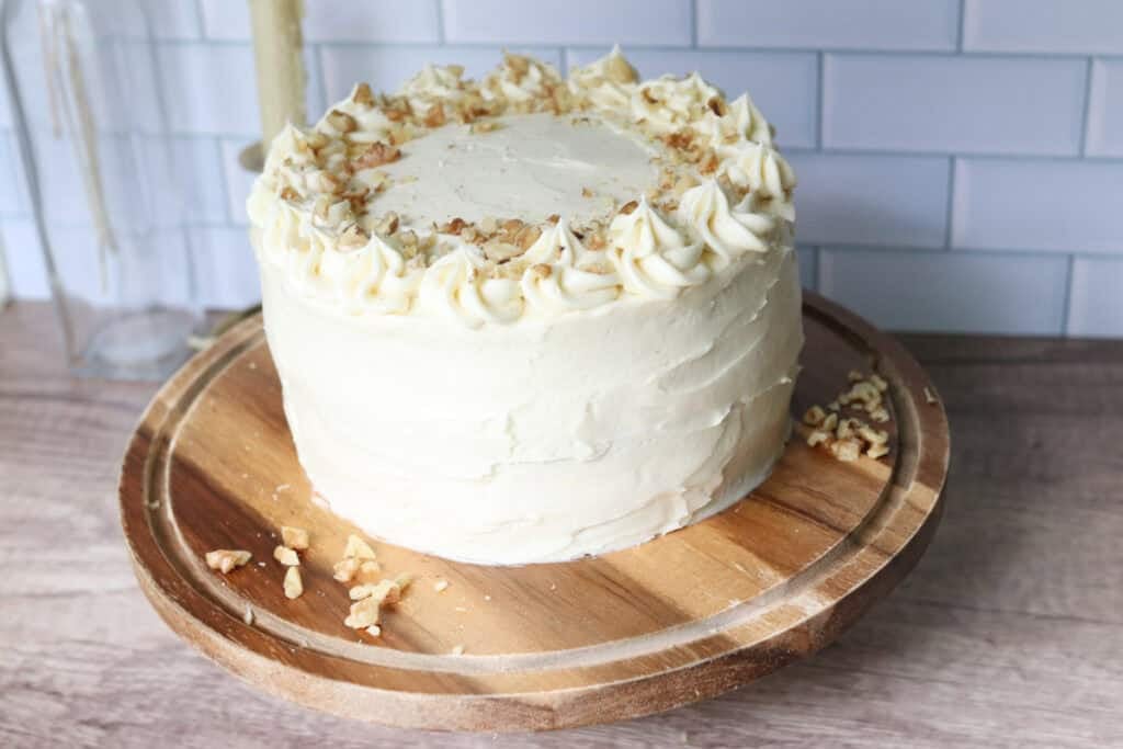 freshly milled carrot cake with cream cheese icing on top and walnuts on top and on wooden cake stand