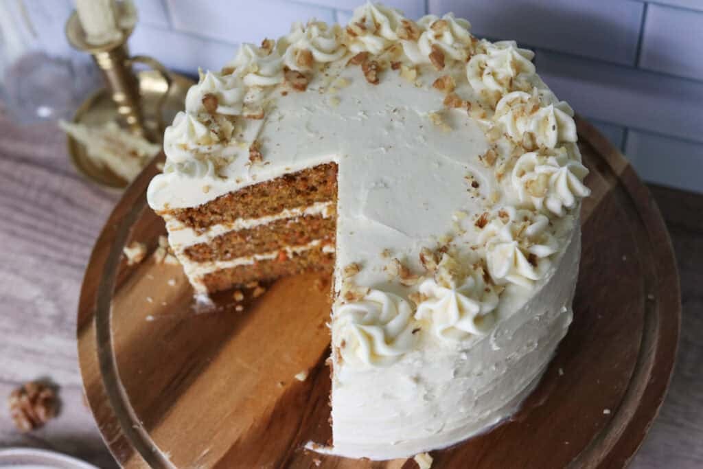 freshly milled carrot cake on a cake stand with cream cheese icing and walnuts on top