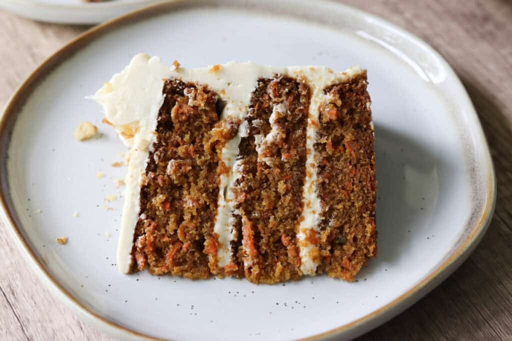 a slice of freshly milled carrot cake with cream cheese icing on a white