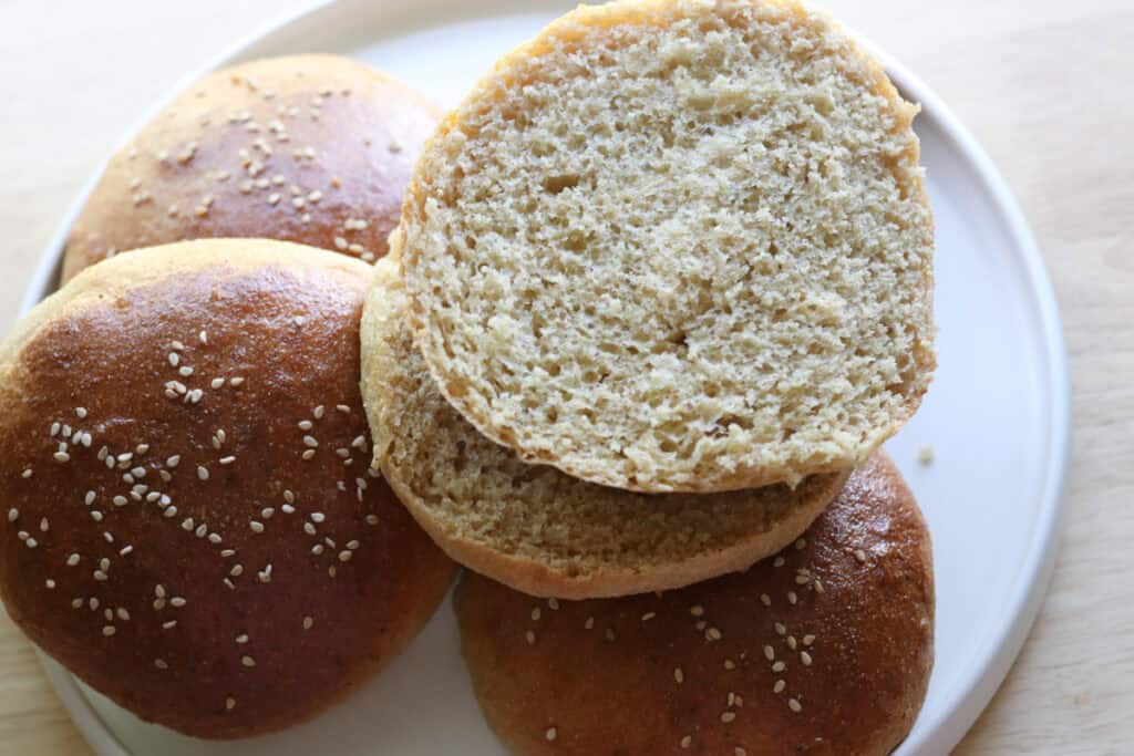 brushing freshly milled brioche burger buns on a white plate with one cut in half