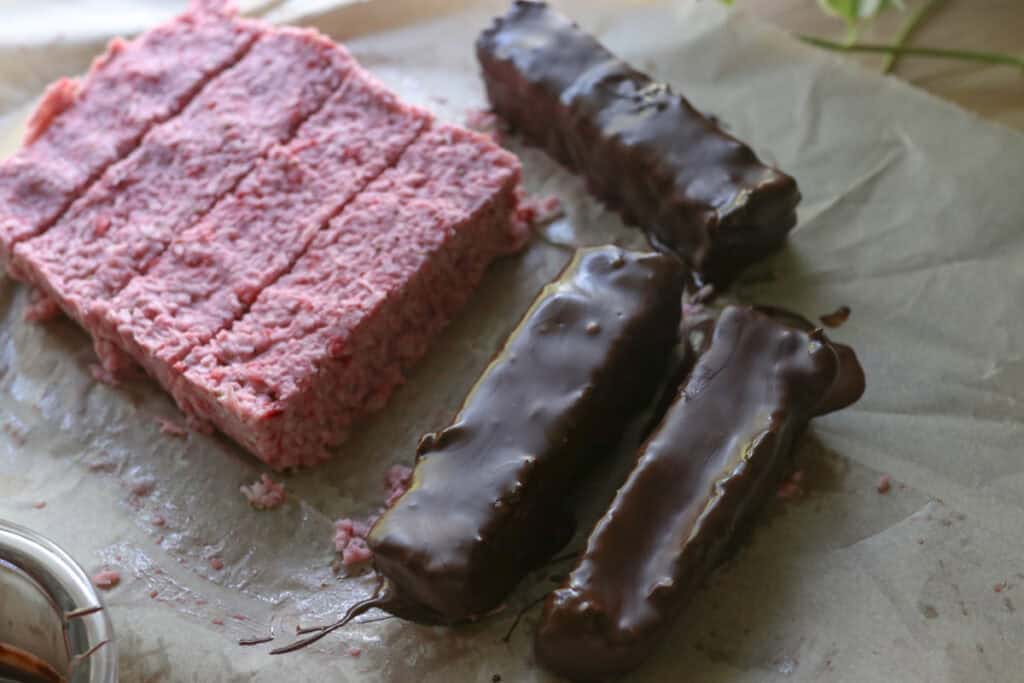  strawberries & cream coconut bars being coated in chocolate on parchment paper