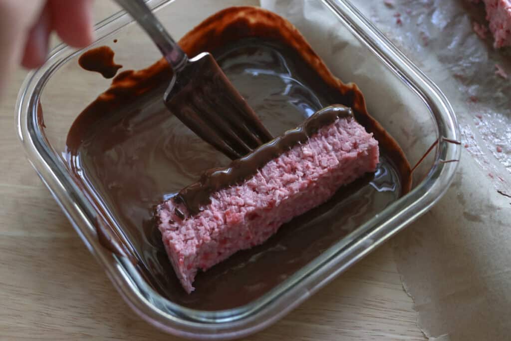 dipping strawberries and cream coconut bars in melted chocolate 