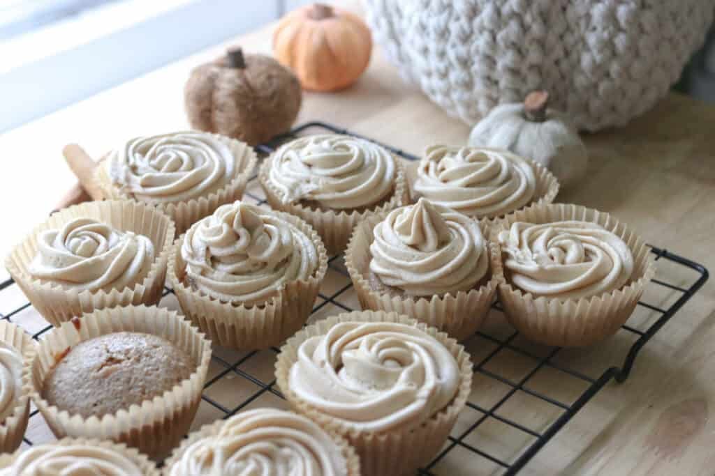 fresh milled apple cider cupcakes with buttercream on a wire rack with mini pumpkins behind it