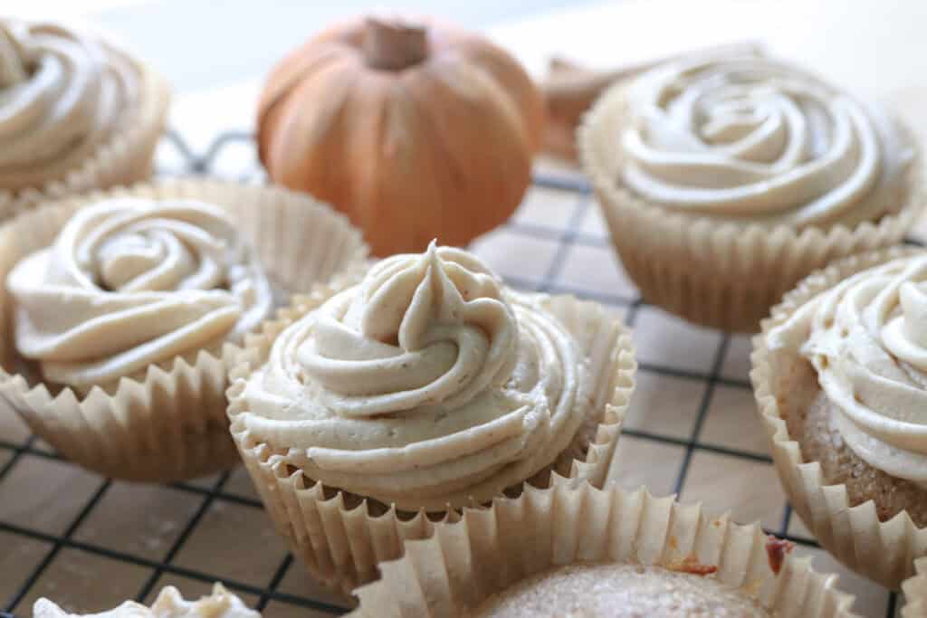 fresh milled apple cider cupcakes with buttercream on top and an orange pumpkin behind it