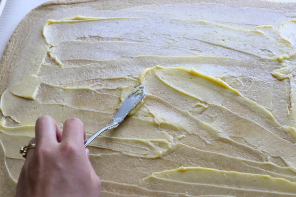 spreading softened butter with a knife on  freshly milled apple cinnamon roll dough