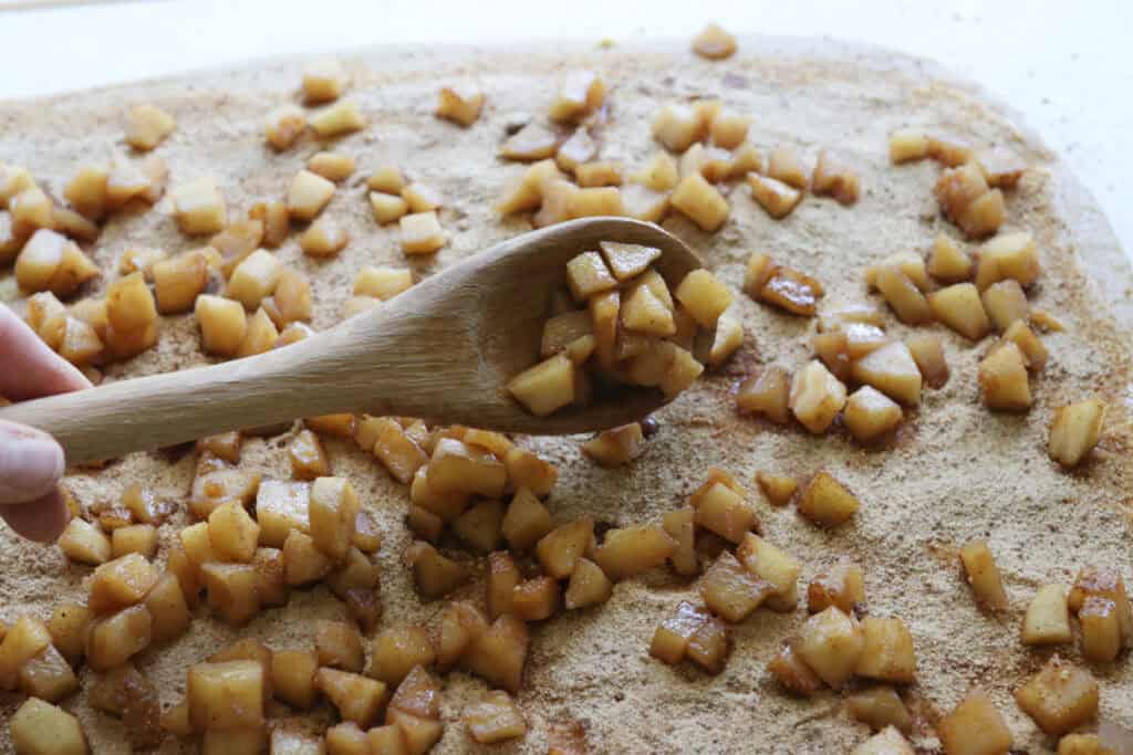 spooning diced apples over top of  freshly milled apple cinnamon roll duogh