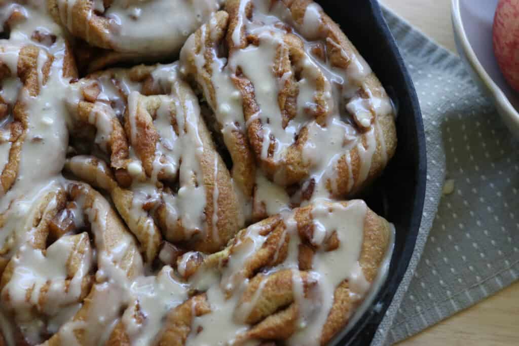  freshly milled apple cinnamon rolls that have icing on them in a skillet