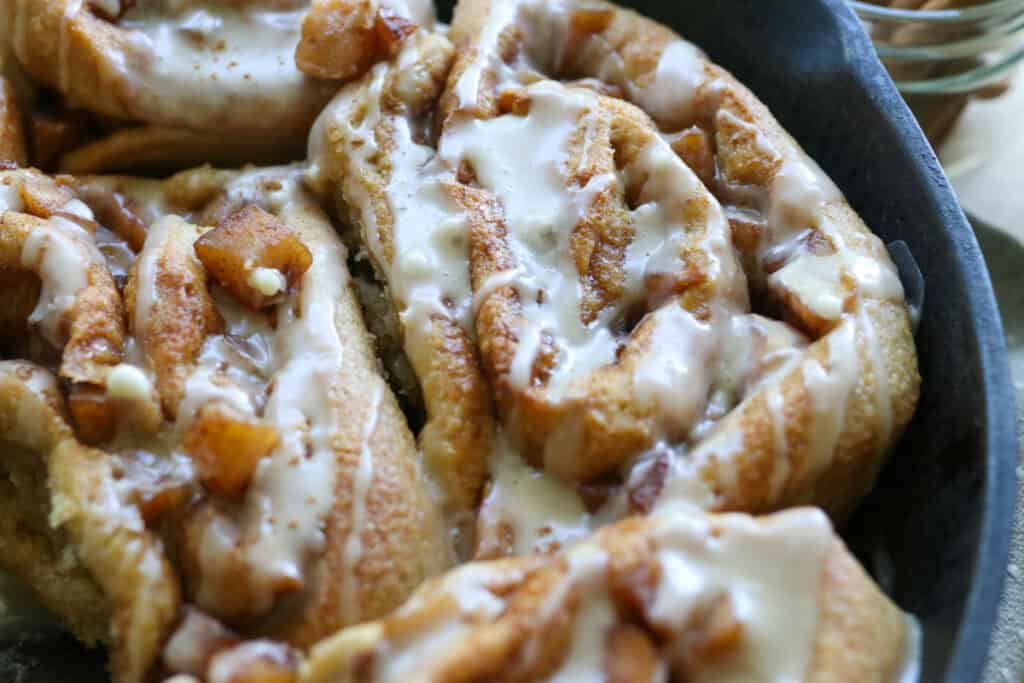 a couple of  freshly milled apple cinnamon rolls with icing on top in a skillet