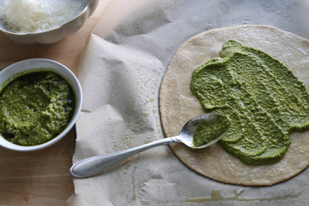 the dough for freshly milled parmesan pesto star bread rolled into a disc and spread with basil pesto sauce