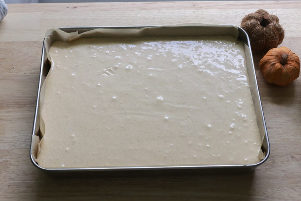 pumpkin cheesecake filling in a baking pan with mini pumpkins beside it