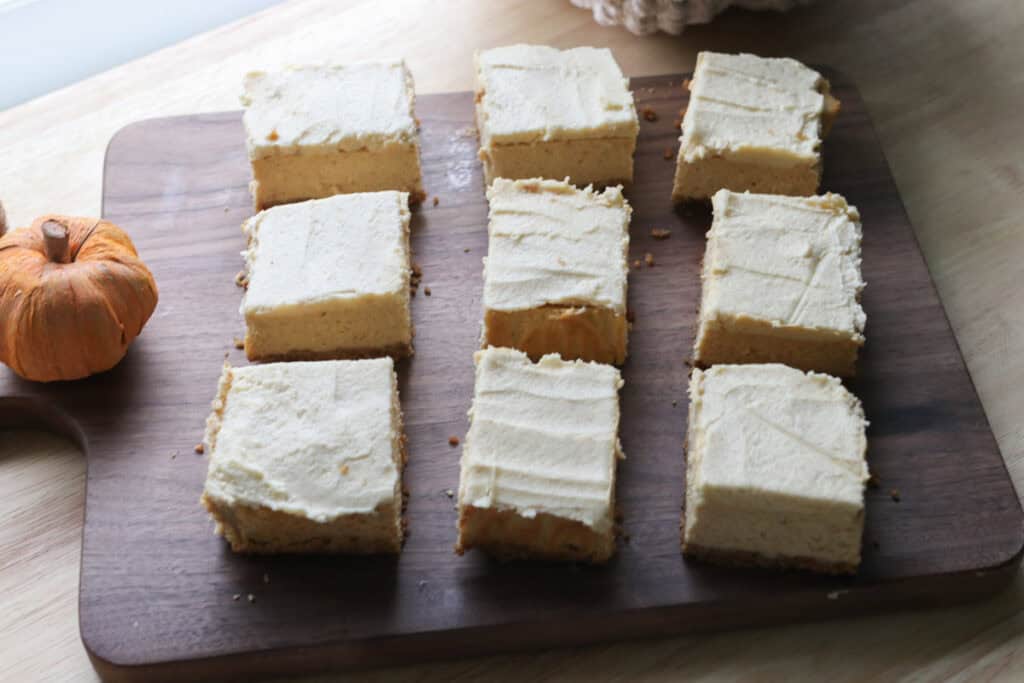 pumpkin cheesecake bars with fresh milled crust on a wooden cutting board with an orange pumpkin