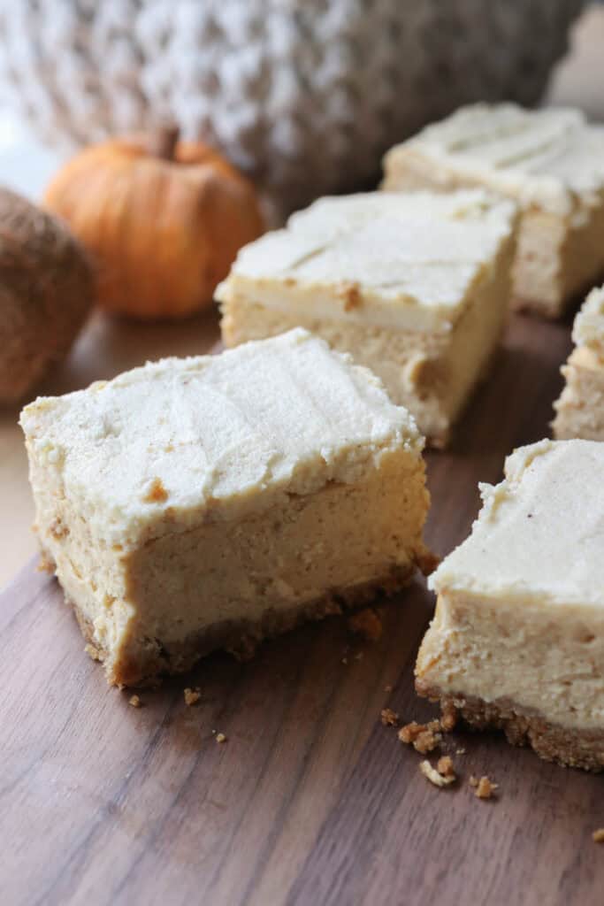 pumpkin cheesecake bars with fresh milled crust and icing on top cut into squares on a wooden board 