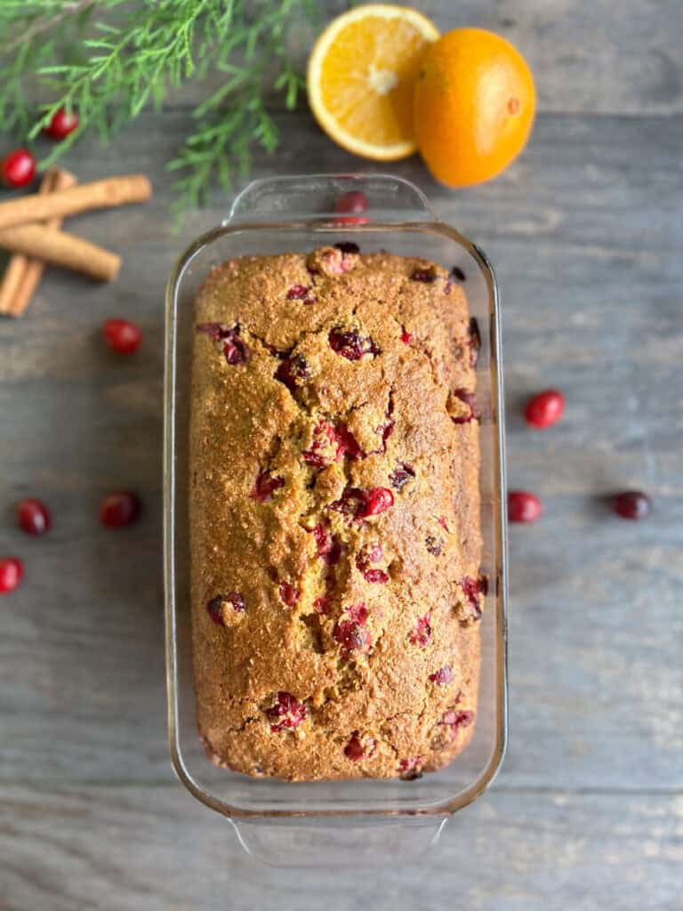 fresh milled orange cranberry loaf in a glass loaf pan with cranberries beside it