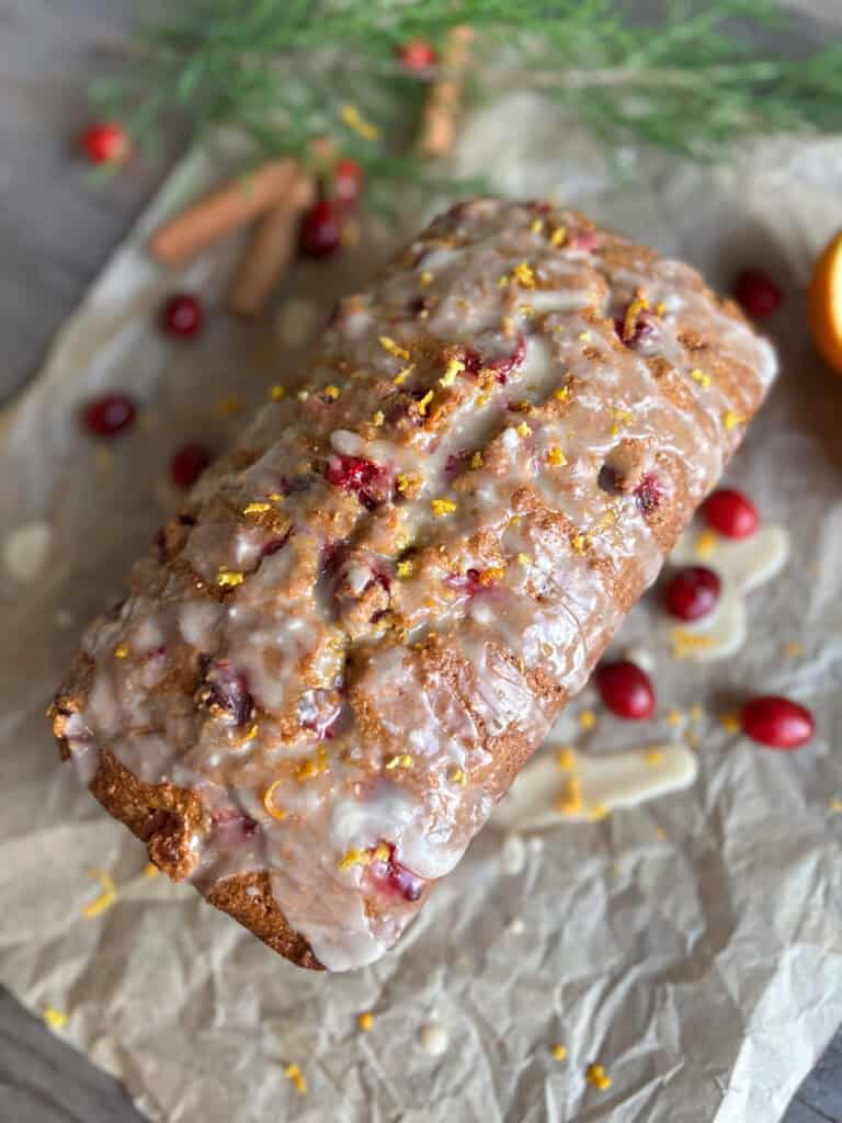 fresh milled orange cranberry loaf covered in icing and orange zest on a piece of parchment paper