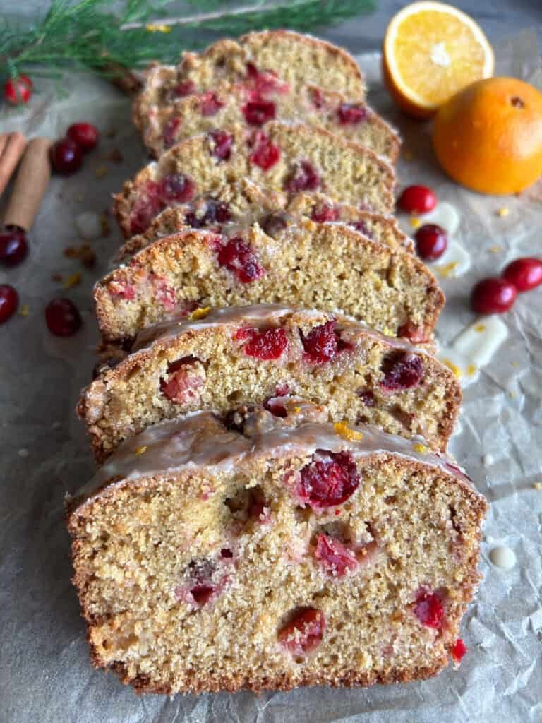 fresh milled orange cranberry loaf that has been cut in slices and has cranberries inside of it and an orange behind it