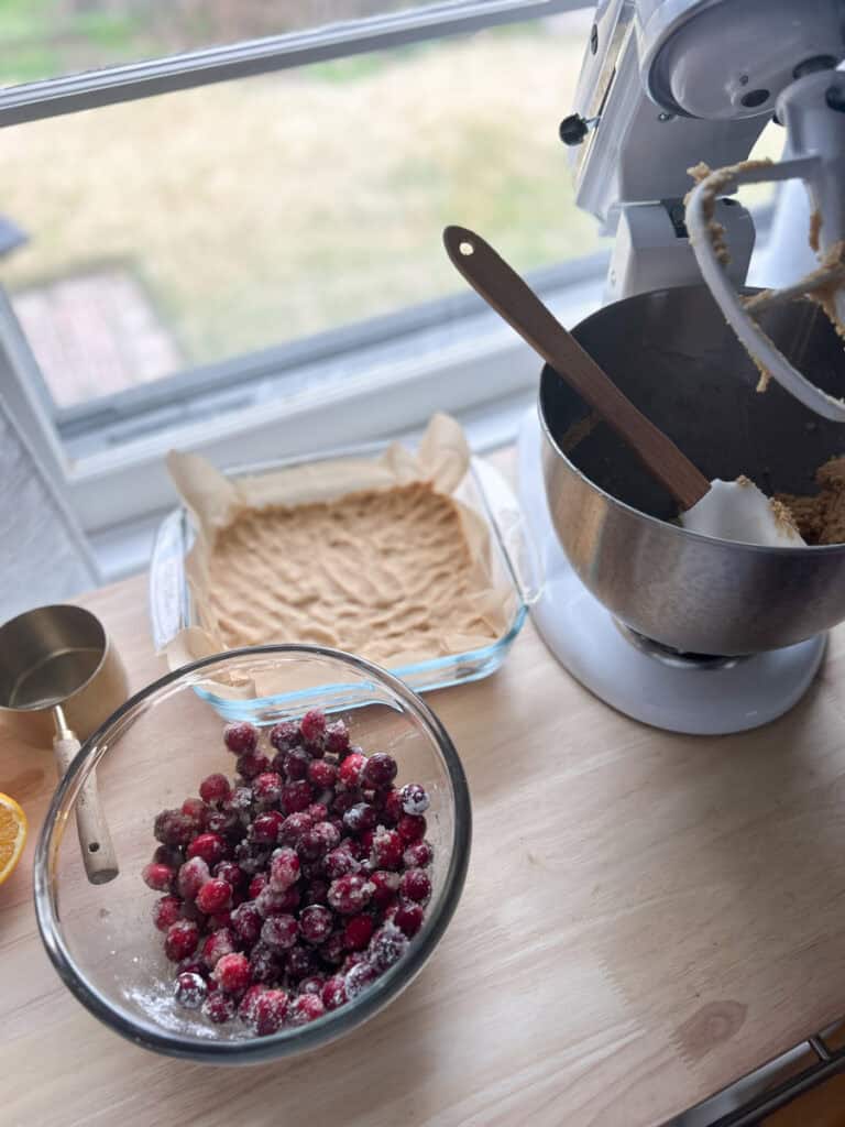dough for Fresh Milled Cranberry Crumble Bars pressed in a pan with cranberries in a bowl 