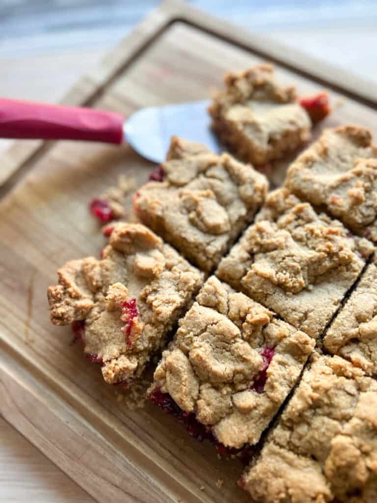 Fresh Milled Cranberry Crumble Bars  on a cutting board cut into squares with a serving spatula