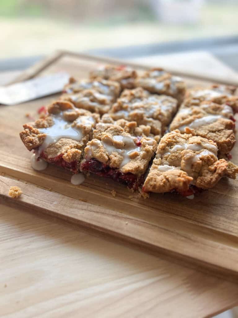 Fresh Milled Cranberry Crumble Bars  with glaze drizzled on top on a wooden board