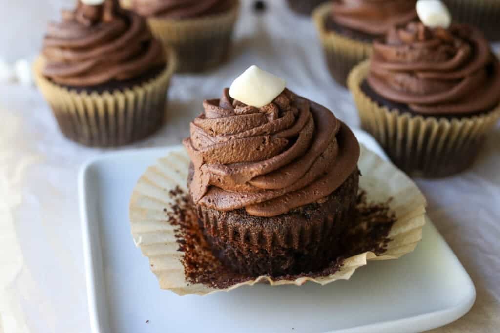 a fresh milled hot cocoa cupcake topped with chocolate buttercream and a marshmalllow on a white plate