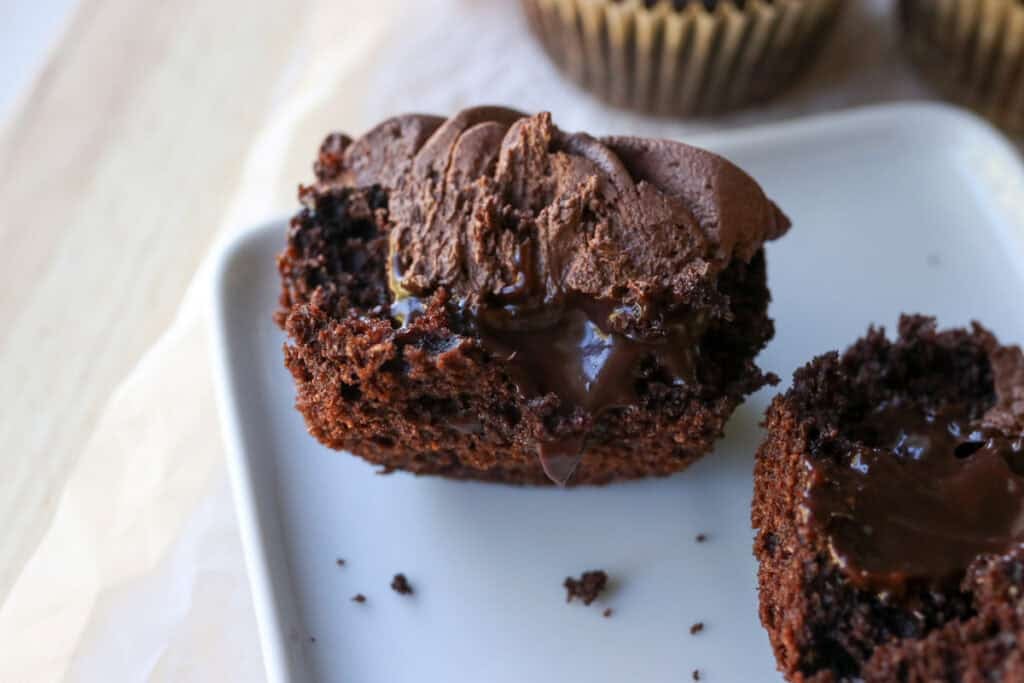 a fresh milled hot cocoa cupcake on a white plate cut in half with chocolate ganache