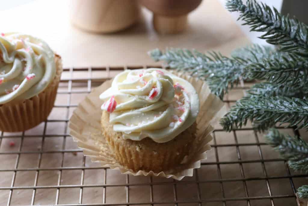 a Freshly Milled White Chocolate Peppermint Cupcake with crushed candy canes on top and cupcake wrapper