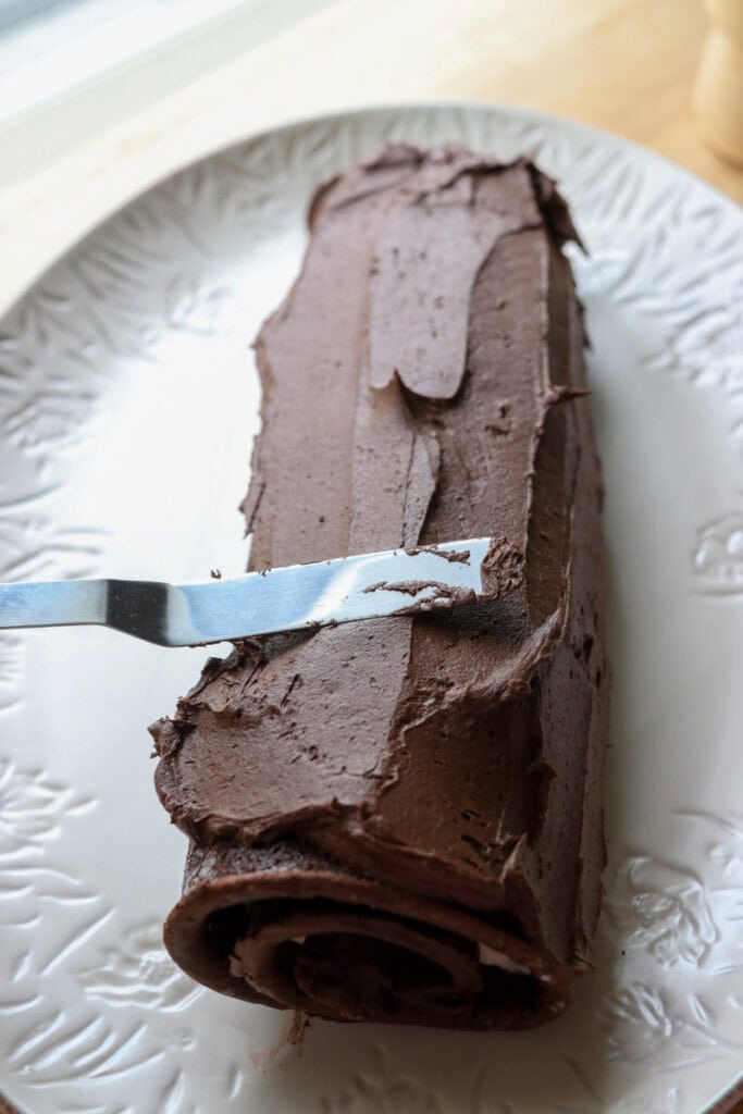 spreading chocolate buttercream over a  freshly milled chocolate yule log cake