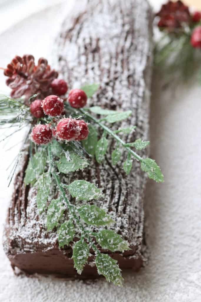  freshly milled chocolate yule log cake covered in powdered sugar on a white plate
