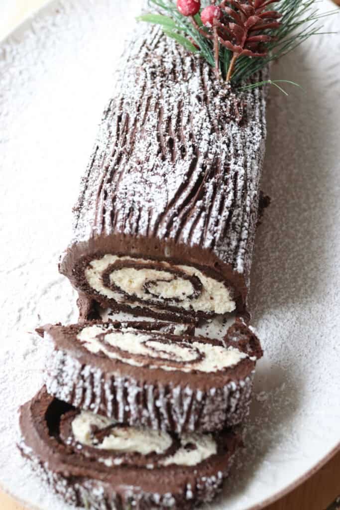 freshly milled chocolate yule log cake cut into swirled slices with chocolate buttercream and powdered sugar