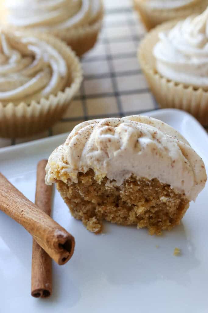 a fresh milled eggnog cupcake cut in half on a white plate with cinnamon sticks