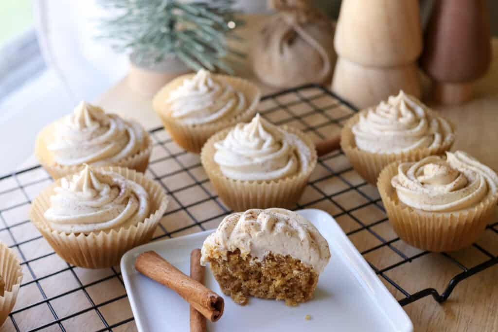 a Fresh Milled Eggnog Cupcake cut in half on a white plate with Cream Cheese Icing and cinnamon sticks