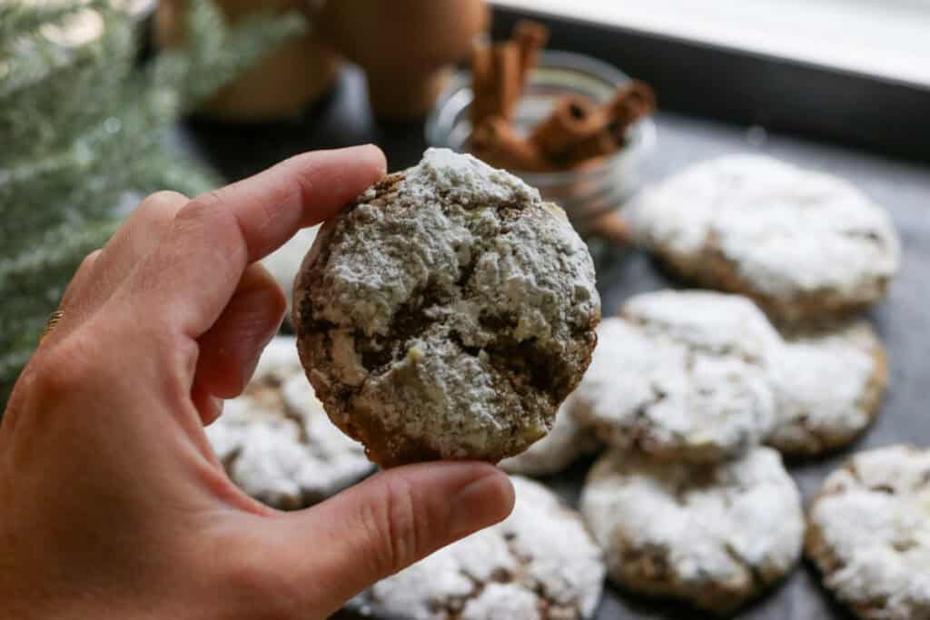 someone holding a freshly milled gingerbread crinkle cookies with more cookies in the background