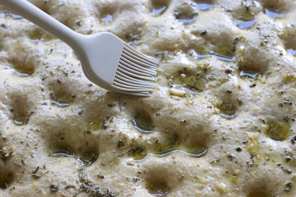a pastry brush spreading garlic oil on top of fresh milled garlic herb focaccia