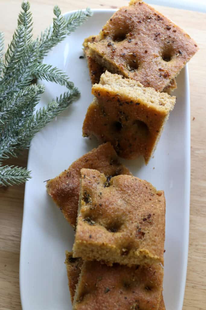 Easy Garlic Herb Focaccia with Fresh Milled Flour on a white plate and a wooden background with trees beside it