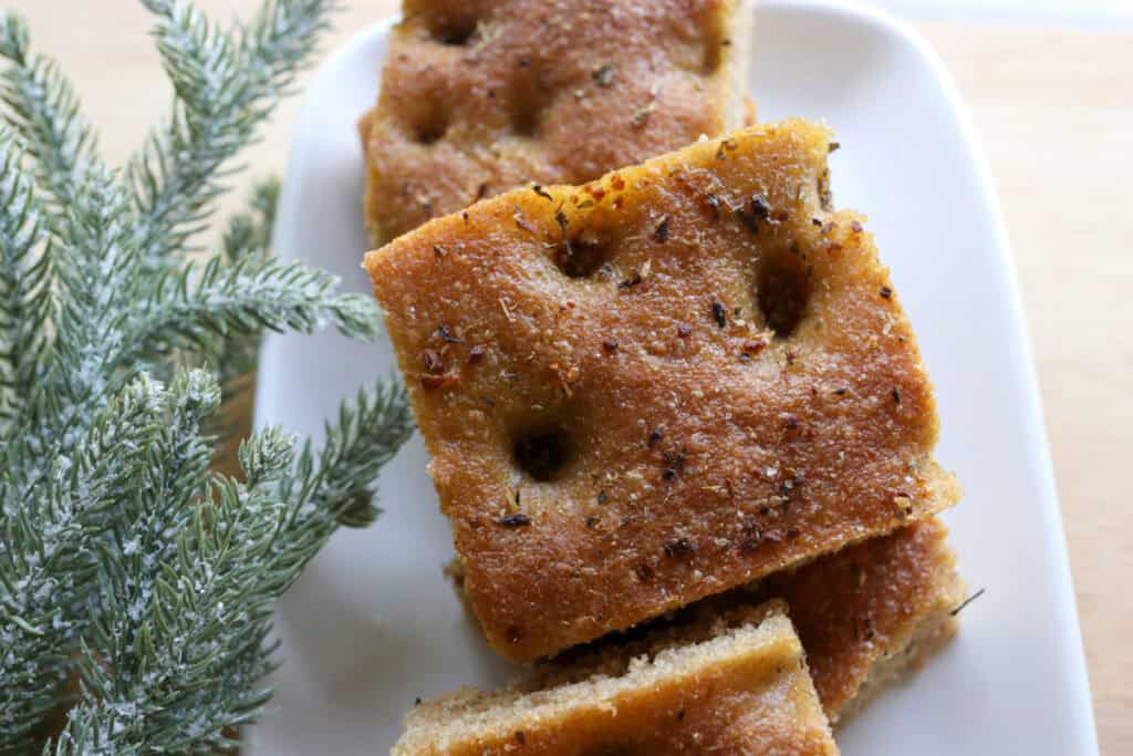 a slice of fresh milled focaccia on a white plate with herbs baked on it