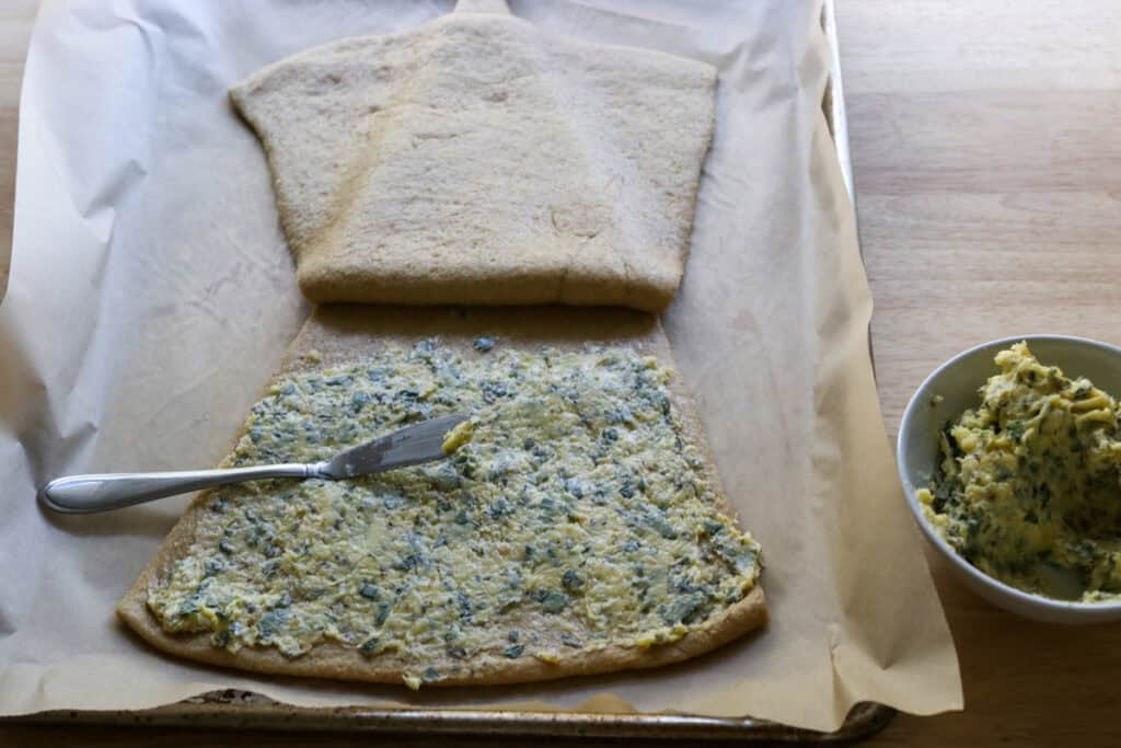 spreading garlic and herb butter on the bottom of a triangle to make Fresh Milled Christmas Tree Garlic and Herb Bread