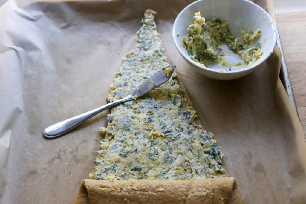 spreading garlic and herb butter on the top of a piece of dough for the Fresh Milled Christmas Tree Garlic and Herb Bread
