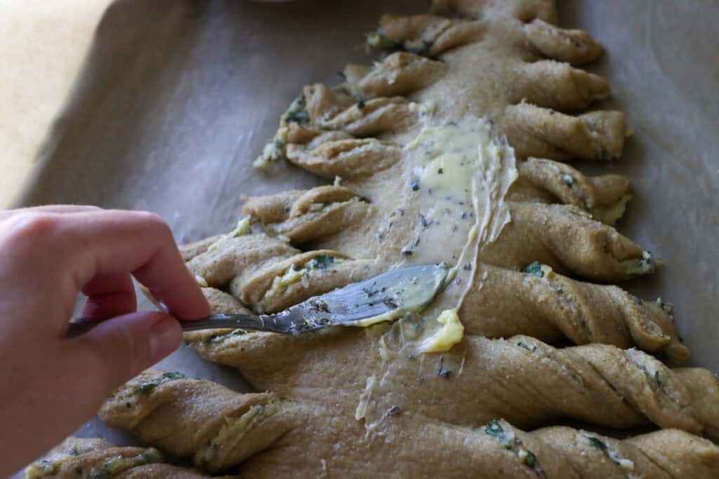 spreading butter with a knife on top of Fresh Milled Christmas Tree Garlic and Herb Bread