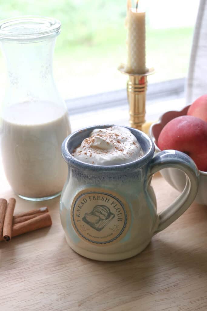 coffee and whipped cream in a blue mug with Delicious Homemade Apple Flavored Coffee Creamer in a jar