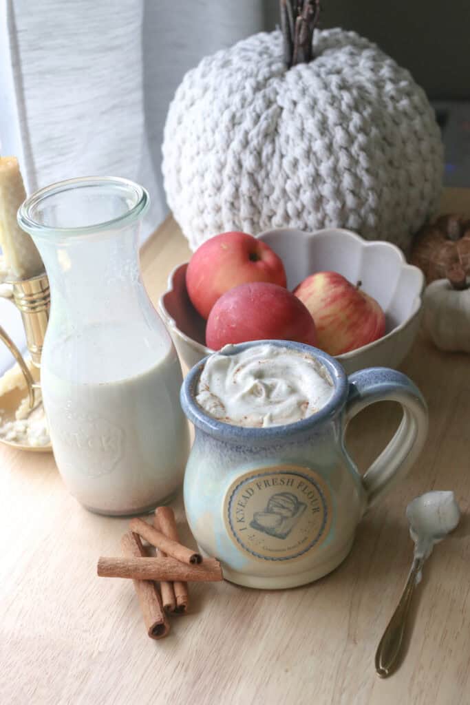 Delicious Homemade Apple Flavored Coffee Creamer in a glass pitcher and coffee and whipped cream in a mug with a spoon and cinnamon sticks