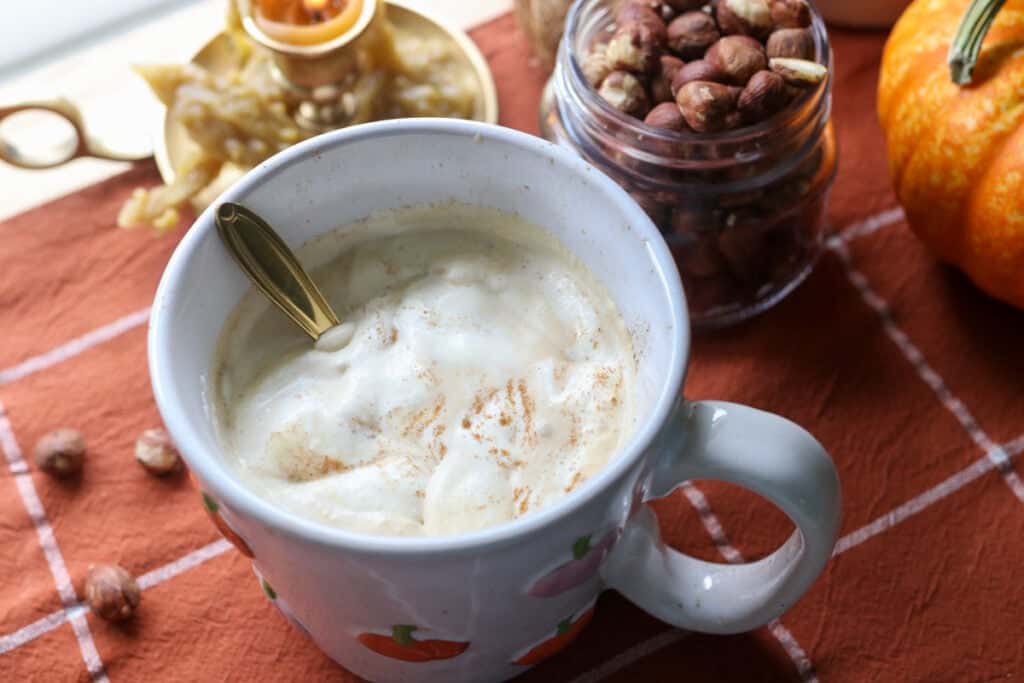 coffee in a mug with naturally sweetened hazelnut coffee creamer and a gold spoon and candle