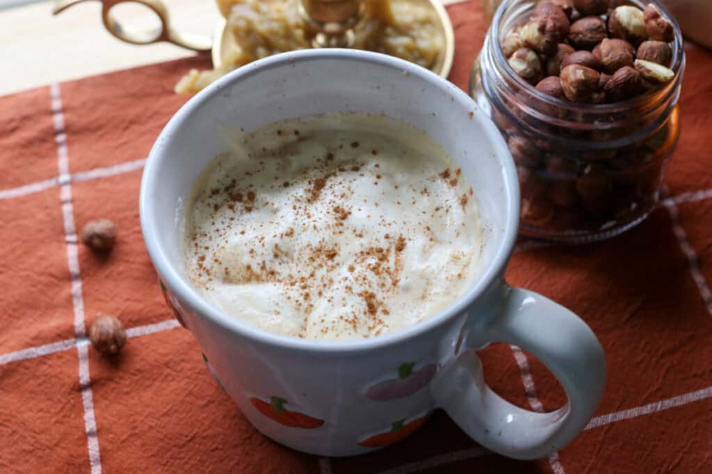 coffee and naturally sweetened hazelnut coffee creamer in a white mug with hazelnuts behind it