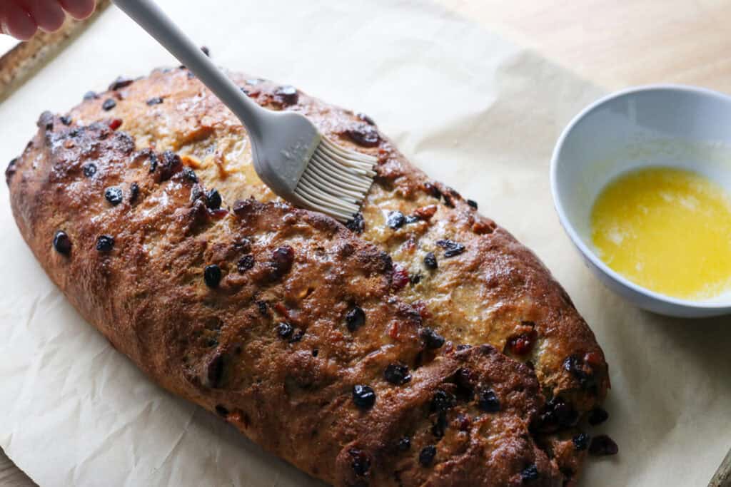 brushing bread over top of fresh milled Christmas Stollen bread