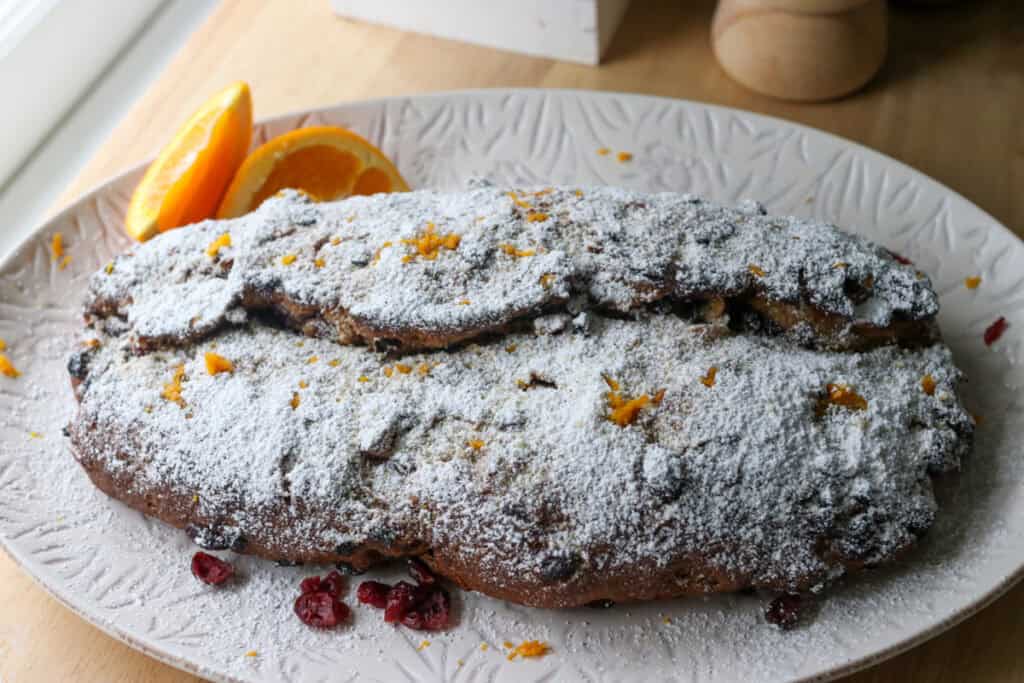 fresh milled Christmas Stollen bread covered in powdered sugar with orange slices and dried berries