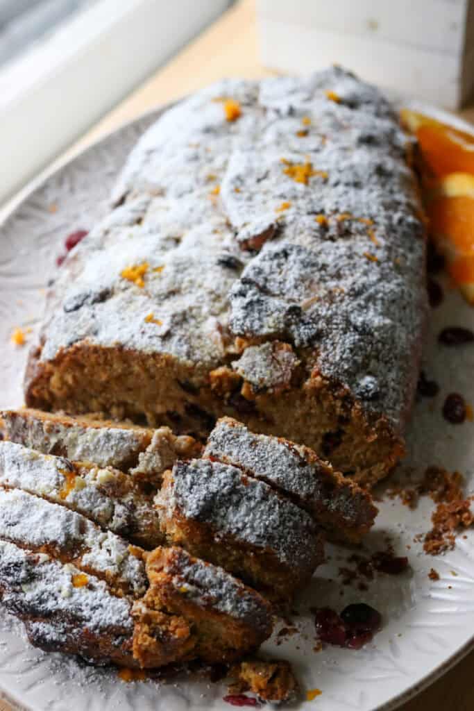 a loaf of fresh milled Stollen bread on a white plate that has been cut into slices